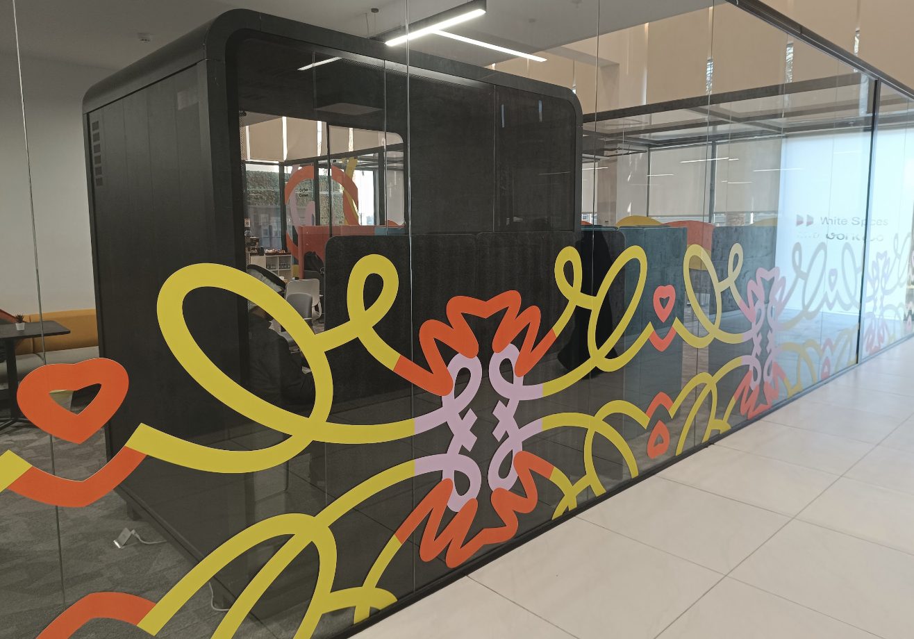 Glass phone booth with a bright squiggle mural at a White Spaces and Work&Co site